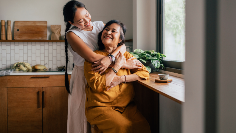 Mother and daughter embracing and smiling at each other in kitchen in front of window.