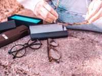 Two pairs of glasses and their boxes are spread out on a sidewalk while a woman holds a third pair.