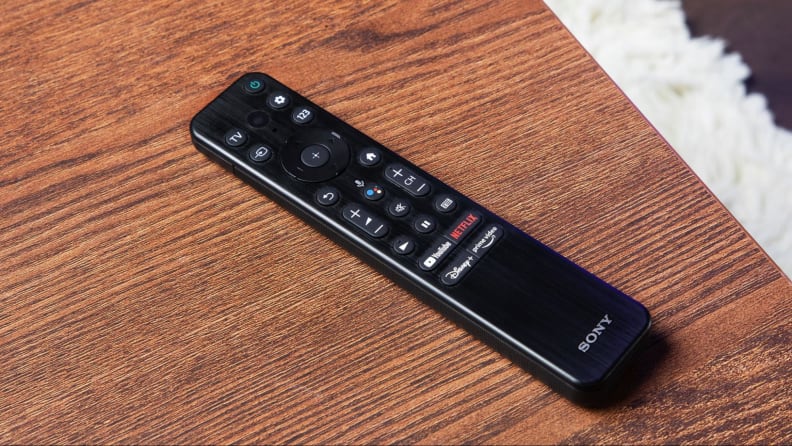 A black Sony television remote sits on a wood table.