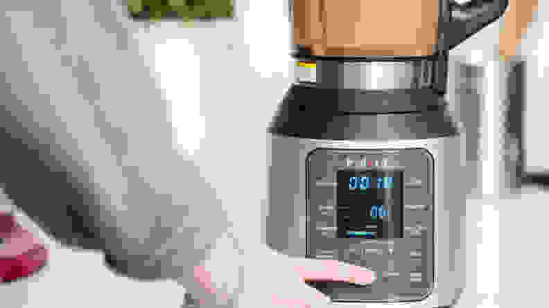 A person pushes a button to set the speed on a blender filled with soup.