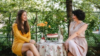 Two women smiling while enjoying tea in a garden.