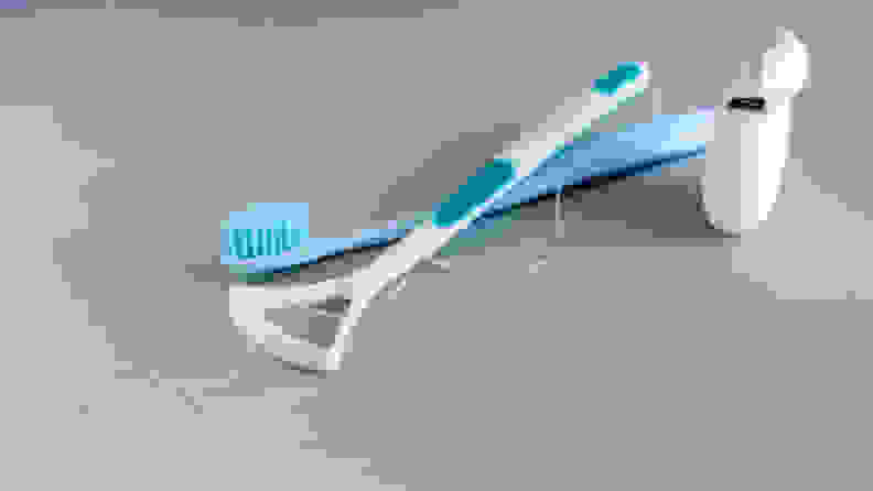 A tongue scraper sitting atop a toothbrush and dental floss.