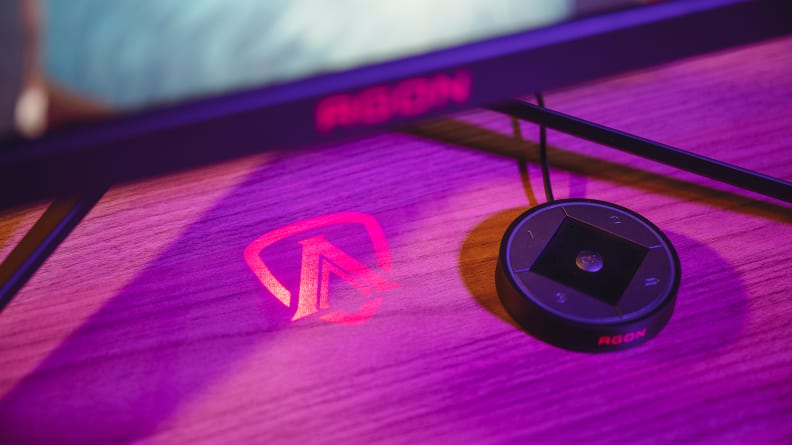 A glowing red logo is projected onto the top of a wooden desk with a black hockey puck-like disc beside it.