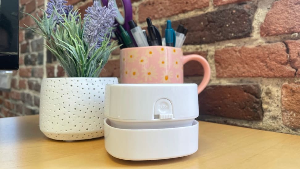 Odistar Desktop Vacuum sitting on top of wooden desk next to mug and potted plant.