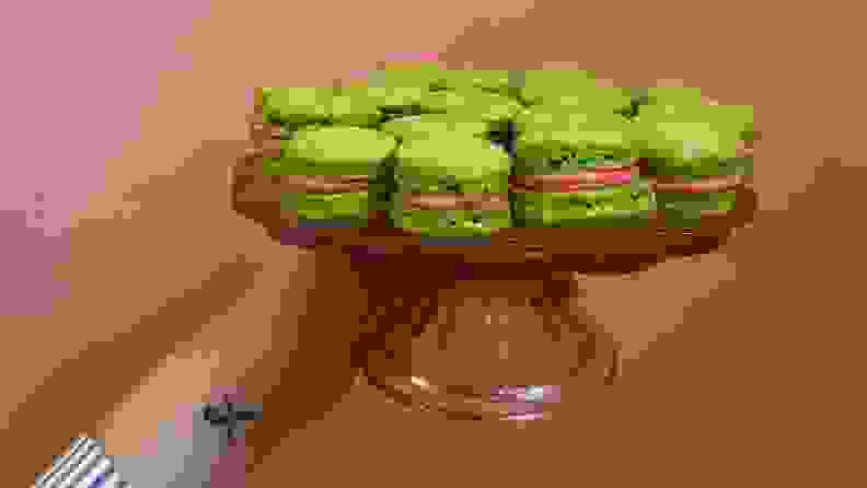 A hand holds a pink cake stand filled with lime green macarons.