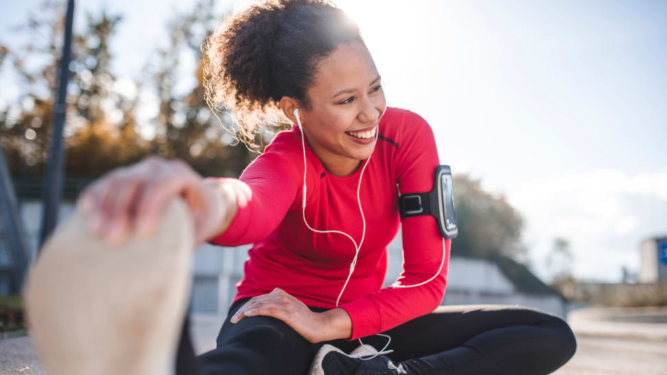 Woman stretching outside wearing headphones and workout clothes.