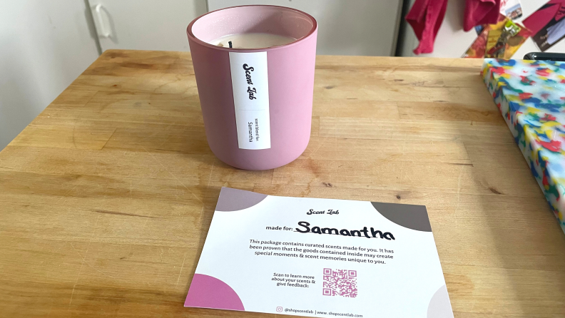 A personalized pink Scent Lab candle on a wooden table next to a personalized Scent Lab Candle card.