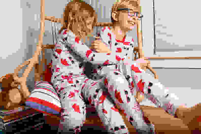 A boy and a girl wearing matching Christmas pajamas sitting in a swing