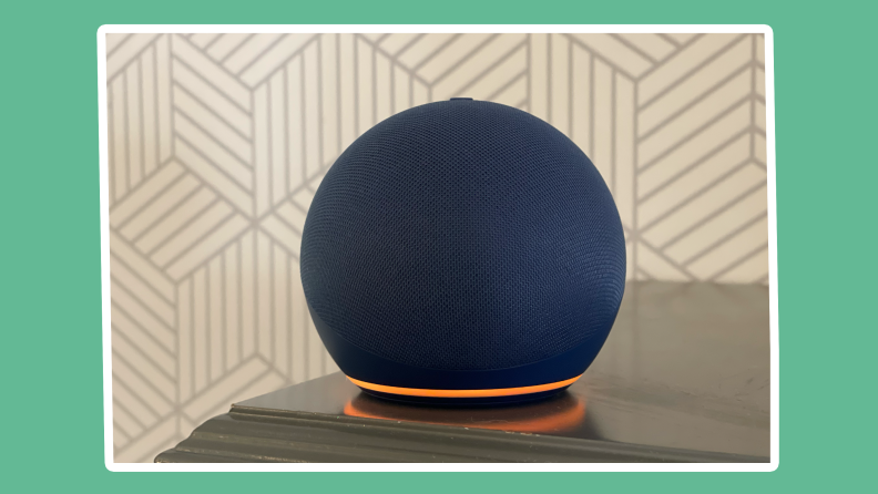 Navy blue 5th generation Amazon Echo Dot virtual assistant speaker sitting on edge of wooden surface indoors with orange LED light .