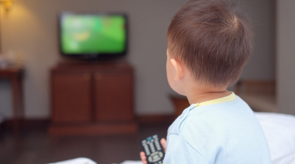 Young child holds remote and looks at a television