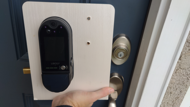 A Lockly Vision Elite held up no a panel, showing its size relative to a door handle.