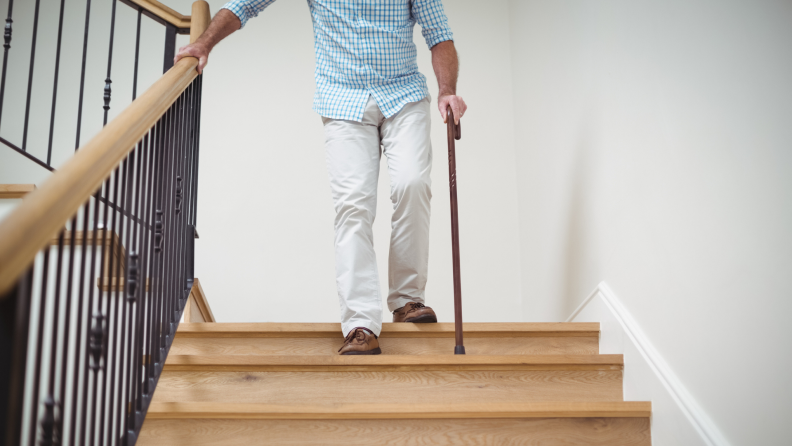 Elderly man using cane to get down set of stairs.