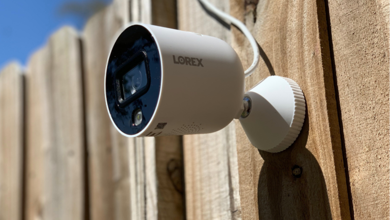 The Lorex Indoor/Outdoor WiFi Security Camera hangs on a fence