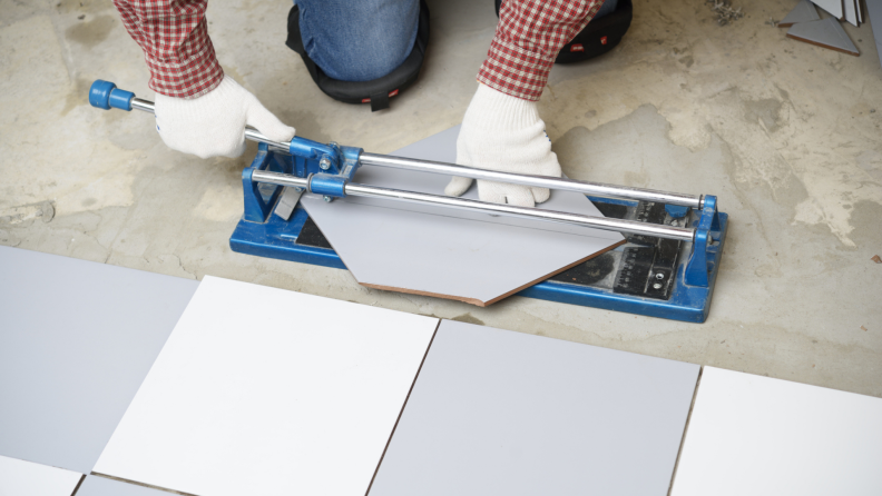 Person using tile cutter on floor to cut tile while installing.