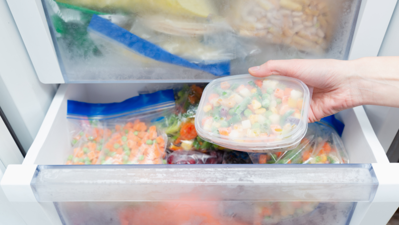 A person removing a container of frozen peas and carrots from the freezer.
