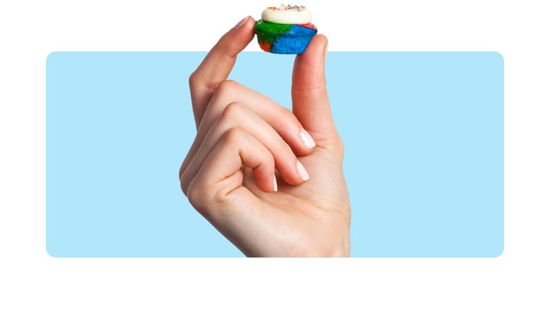 A hand holding up a mini cupcake in front of a background.