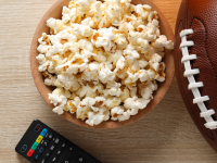 A bowl of popcorn on a table with a football and TV remote