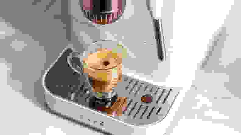 Close-up of Affetto machine pouring crema-topped espresso into a glass shot mug with a drop on top.