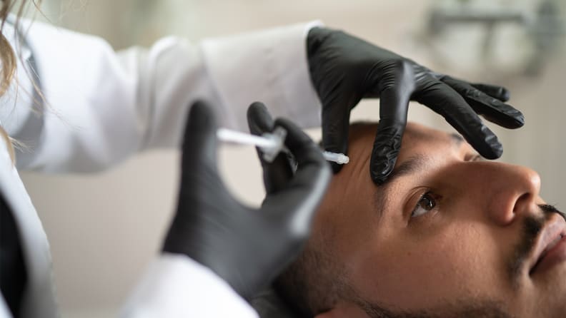 A closeup on a person's forehead with a doctor pinching the skin and injecting a needle into it.