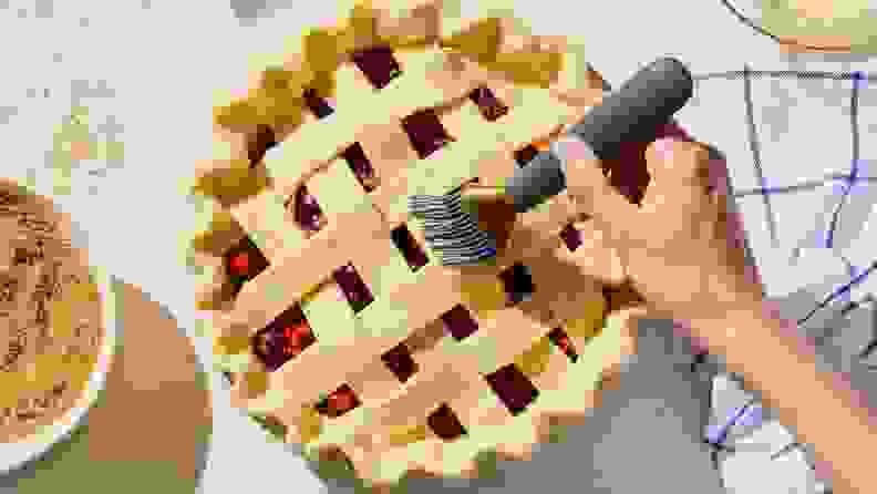 A hand uses a pastry brush to spread melted butter across the lattice crust on a homemade pie.