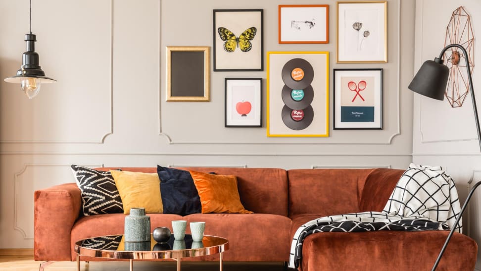 Living room with orange couch with throw pillows, a dining table, a black lamp, and a gallery wall with six art frames