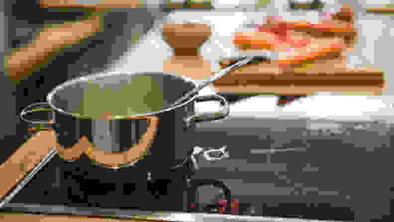 A pot sits on an induction stovetop with a cutting board with carrots on it in the background.
