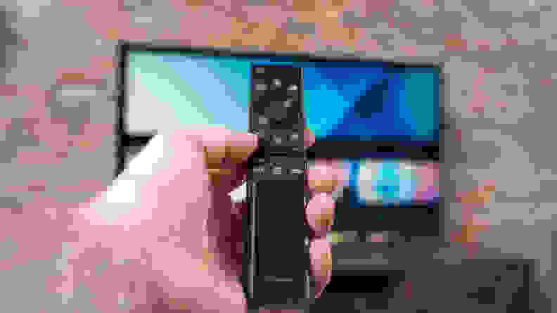 A man holds the Samsung TV remote in front of the screen