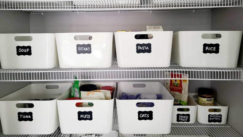 White organization bins with black chalkboard labels inside of a kitchen pantry of home.