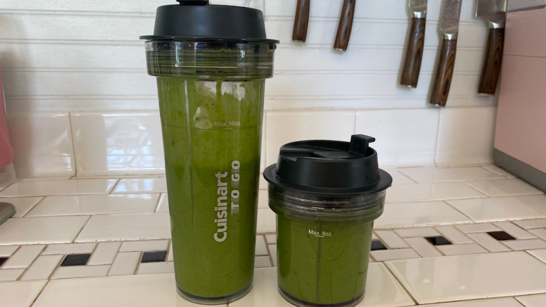 Two different sized Cuisinart travel mugs with lids and green smoothies inside side by side.