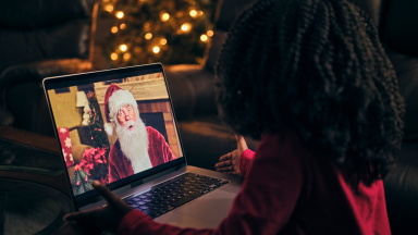 A young child looking at a laptop showing an image of Santa Claus.