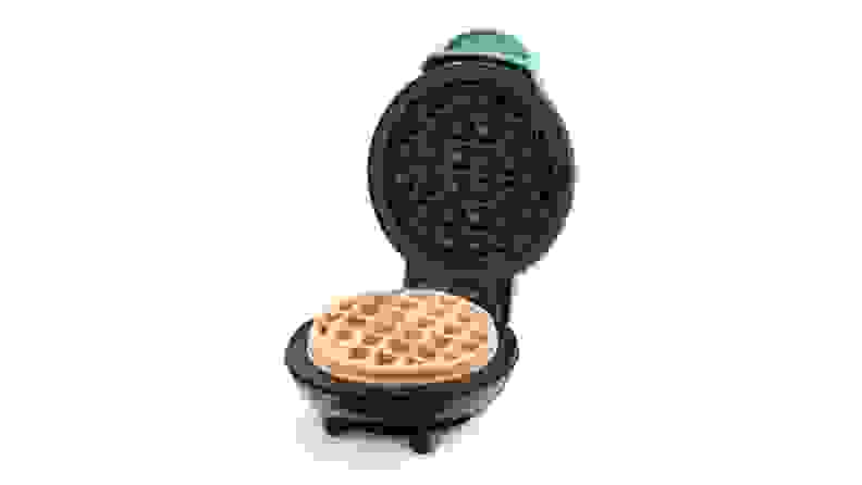 A light blue mini waffle maker sits with its top open to reveal a cooked mini waffle inside.