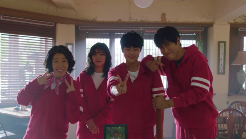 Group of four people in red tracksuits pose together in front of camera smiling.