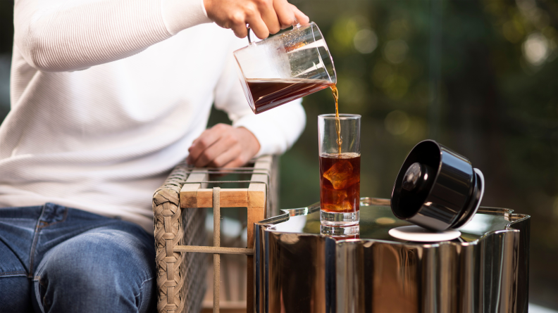 A person is pouring coffee from a VacOne coffee maker into a glass.