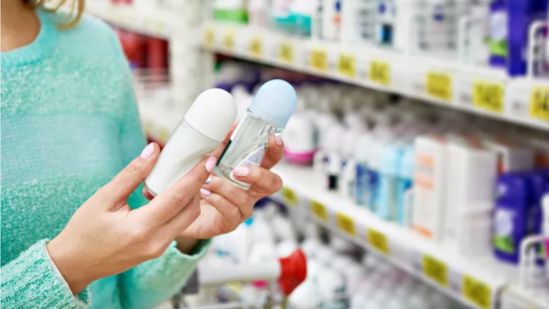 A woman shopping in the deodorant aisle with two deodorant stick in her hand.