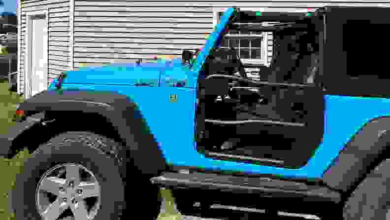 A wide profile view of a light blue Jeep with the Rugged Ridge Fortis Tube Doors installed, in front of a house.