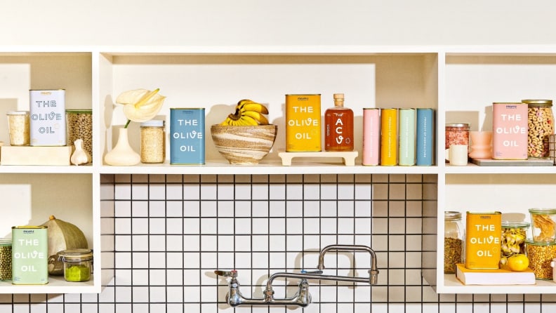 Open kitchen shelving filled with Pineapple Collaborative olive oil and other miscellaneous products.