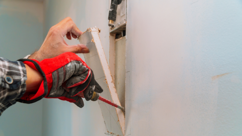 person cuts hole in drywall for a patch