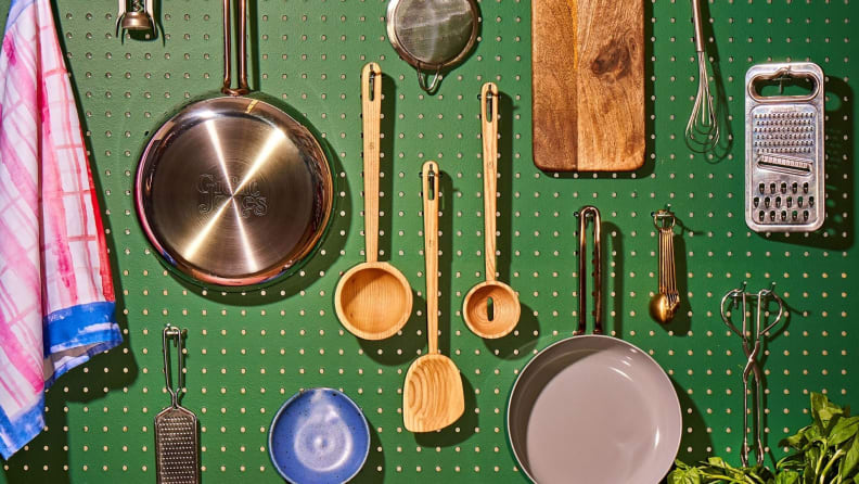 A green peg board displaying three wooden utensils, various cookware, and other miscellaneous kitchen gadgets.