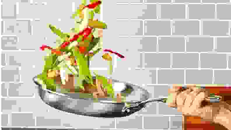 A chef tosses vegetables from a skillet.