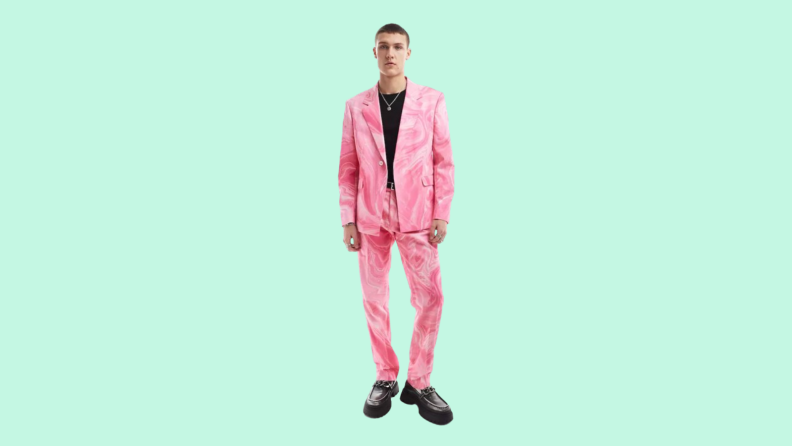 Man in pink suit jacket and pants with black shirt and shoes against teal background