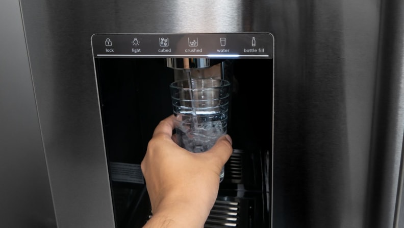 Person using water dispenser on the Bosch B36FD50SNS French-door Refrigerator to pour water into bottle.