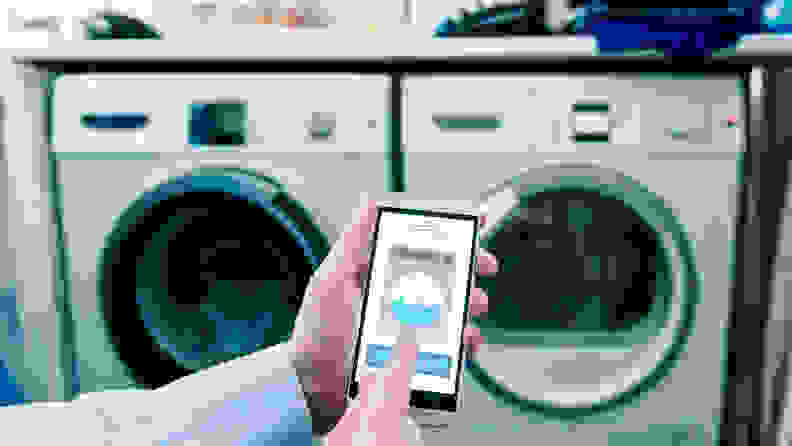 A shot of a hand holding a cell phone up in front of a laundry center.