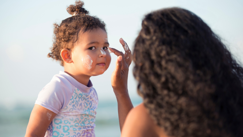 A photo of a woman applying sunscreen to a toddler's face.