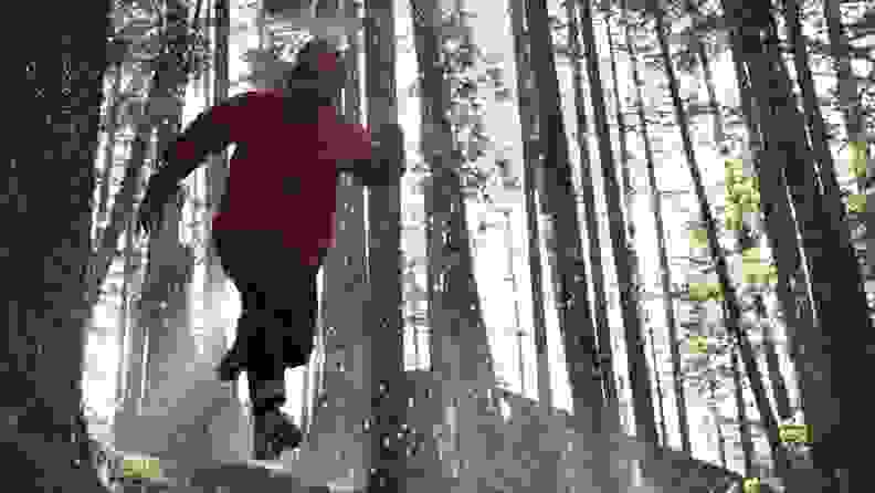 Man running in woods wearing red Gore-Tex jacket.