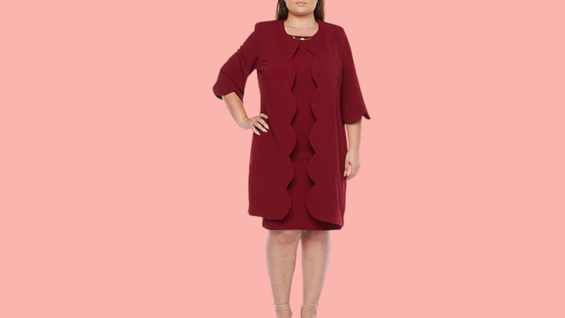 A woman wears a burgundy dress with a matching jacket with three quarter sleeves and a scalloped edge.