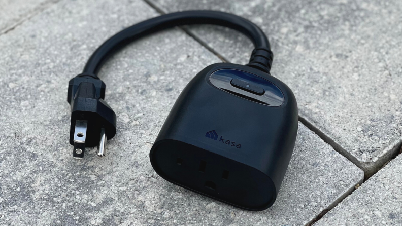 The Kasa Outdoor Smart Dimmer Plug sits on a paver patio