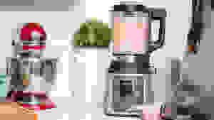 A person blends a smoothie in a blender on a countertop surrounded by other kitchen items.