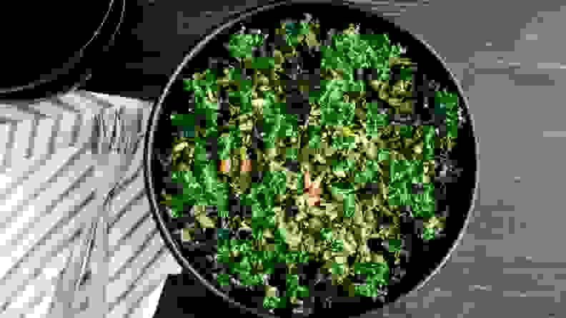 Kale salad in a black bowl, sitting on a wooden surface.
