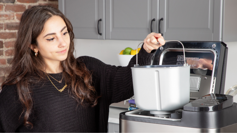 A person lifting the baking bin from the bread maker.