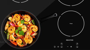 A cast-iron frying pan with shrimp and vegetables sits on an induction stovetop